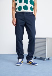 Pantaloni bleu marin, croi ajustat, dintr-un amestec de bumbac. Asortați cu teniși albaștri cu dungi galbene și șireturi albe. Design modern, ușor.