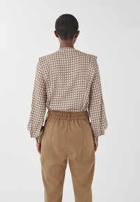 Blusa a fantasia con maniche a sbuffo, base beige e accenti scuri. Abbinata a pantaloni beige a vita alta con un fit rilassato e cintura elastica.