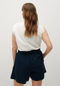 Maglietta bianca senza maniche abbinata a pantaloni blu navy. I pantaloni hanno una vita elastica e una vestibilità ampia, realizzati in un tessuto morbido.