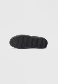 Semelle de chaussure en caoutchouc noir avec un motif en chevrons, finition texturée et bords arrondis, conçue pour l'adhérence et la durabilité.