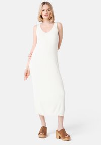 Knit white midi dress with a scoop neckline and ribbed texture, paired with brown clogs featuring a wooden platform and gold studs.