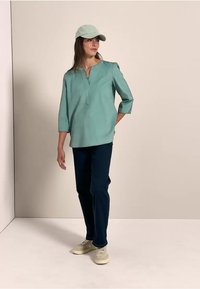 Top verde menta con maniche a tre quarti, pantaloni blu navy e sneakers chiare, completato da un cappellino verde menta abbinato. Design semplice, senza motivi.