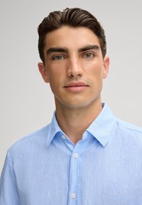 Lichtblauw, kortmouw, knoopshirts gemaakt van textuurstof. Voorzien van een klassieke kraag en witte knopen.