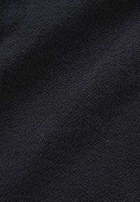 Zbliżenie na czarną tkaninę o delikatnym, fakturowanym splocie z subtelnymi ukośnymi fałdami tworzącymi wariacje światła i cienia.