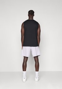 T-shirt sans manches noire associée à un short violet clair, des chaussettes blanches et des baskets. Tissu lisse, coupe décontractée et design minimal.