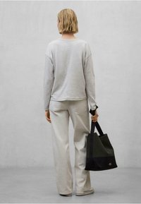 Světle šedý top s dlouhým rukávem a off-white široké kalhoty. Tmavě zelená a černá taška přes rameno s kontrastními texturami. Jednoduchý a minimalistický design.