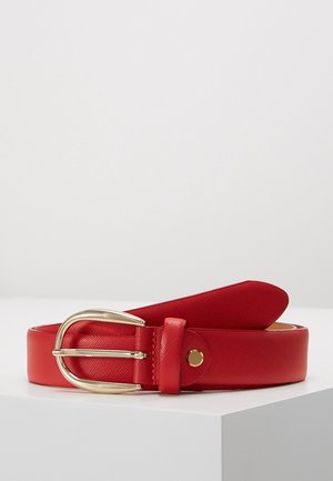 Punainen nahkavyö teksturoidulla pinnalla, kullanvärisellä pyöreällä soljella ja kultaisella niittikoristeella, kierrettynä valkoisella pinnalla.