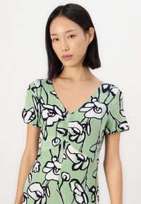 Rochie verde cu imprimeu floral în alb și negru, cu mâneci scurte, decolteu adânc în V și detalii pliate în față.