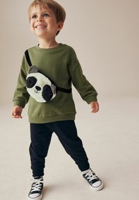 Grøn sweatshirt, sorte sweatpants og sorte sneakers med hvide såler. Har en blød panda crossbody taske med sort og hvidt accent.