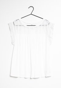 Top bianco con una vestibilità ampia, caratterizzato da un corpetto in pizzo testurizzato e maniche corte. La camicia è appesa a un appendiabiti nero su uno sfondo bianco.