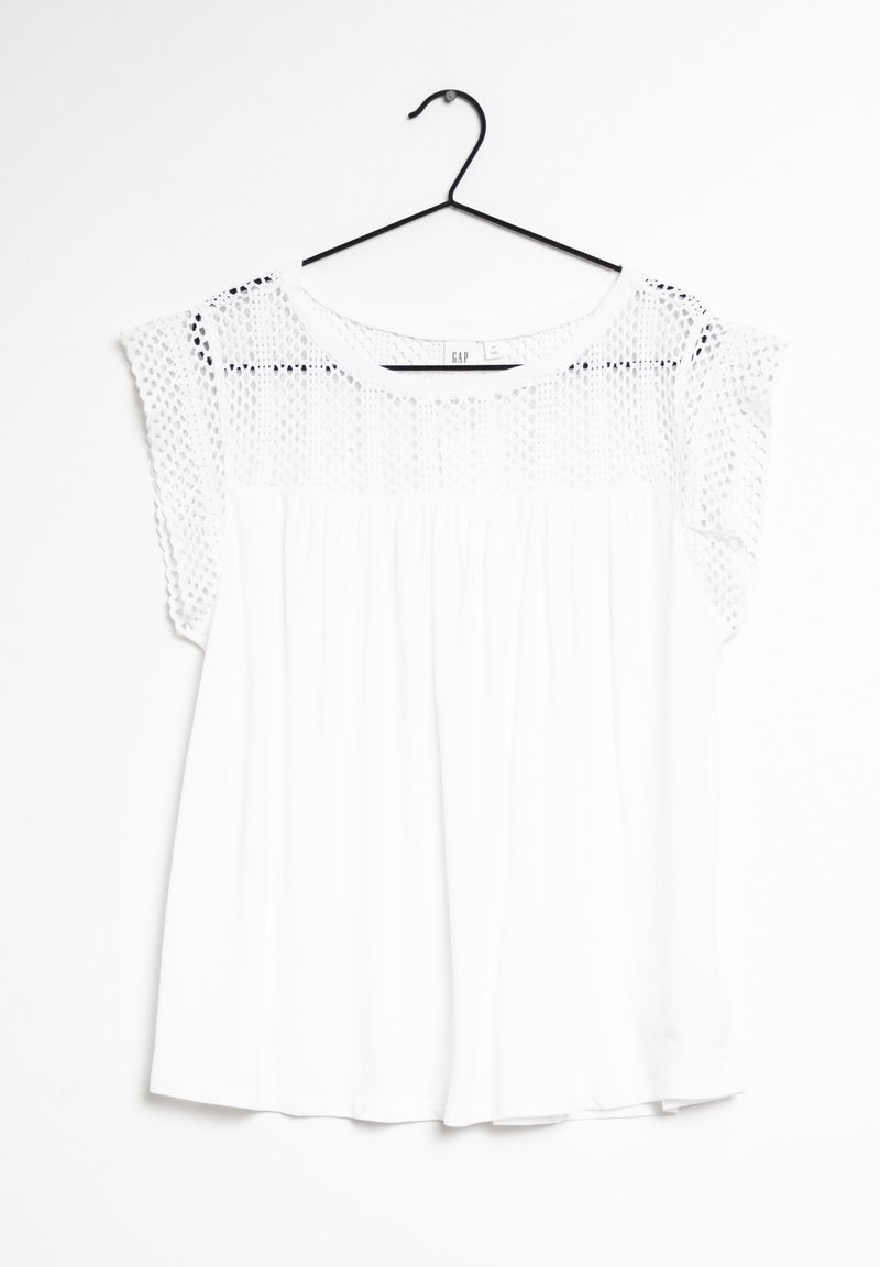 Top bianco con una vestibilità ampia, caratterizzato da un corpetto in pizzo testurizzato e maniche corte. La camicia è appesa a un appendiabiti nero su uno sfondo bianco.