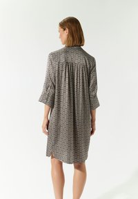 Abito a fantasia bianco e nero con maniche a tre quarti, vestibilità rilassata, piccole fessure laterali e dettagli arricciati sul retro.