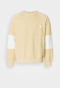 Felpa leggermente beige con una piccola tasca sul petto, pannelli bianchi sulle spalle, polsini a costine e scollatura a girocollo. Tessuto morbido con una vestibilità casual.