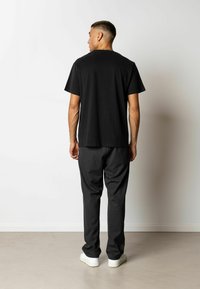T-shirt en coton noir à manches courtes, coupe décontractée, présenté avec un pantalon gris foncé et des baskets blanches, vu de dos.