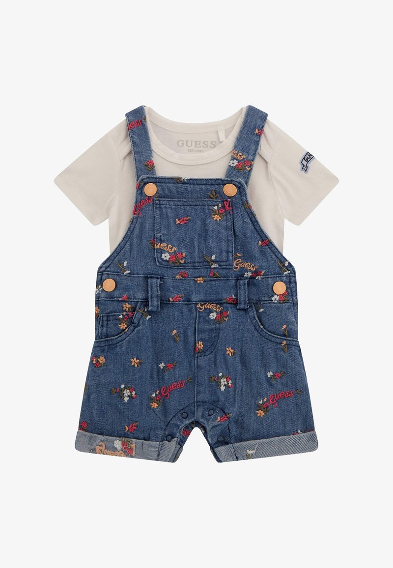 Salopette en denim avec broderie florale, bretelles ajustables et boutons en cuivre. Associée à une chemise blanche à manches courtes. Les shorts présentent des poignets retroussés.