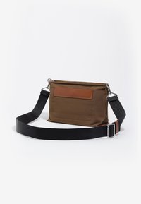 Bolso bandolera de tela marrón con detalle de cuero, correa negra ajustable, herrajes plateados, forma rectangular plana y cierre de cremallera.