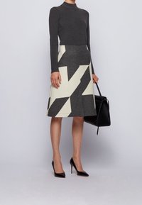 Haut gris à col roulé côtelé associé à une jupe mi-longue avec un motif géométrique audacieux en noir et blanc. Talons aiguilles noirs et sac.