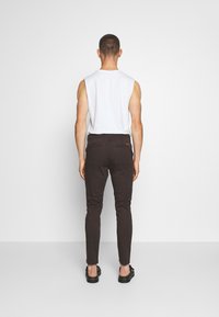 Mustat slim-fit-housut, joissa on kaksi takataskua, yhdistettynä valkoiseen hihattomaan paitaan ja mustiin sandaaleihin. Kangas näyttää sileältä ja kevyeltä.