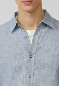 Lichtblauw gestreept shirt met een button-down kraag, een voorpaneel en bruine knopen. De stof lijkt zacht met een subtiele textuur.