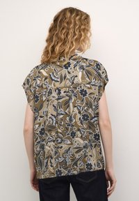 Blusa con motivo floreale in tonalità terrose di marrone, blu e crema. Maniche corte, vestibilità ampia, con dettaglio di piega sul retro e orlo arrotondato.