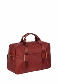 Borsa da viaggio in nylon rosso con manici doppi, chiusura a zip e una tasca piatta su un lato. Presenta una superficie liscia e cuciture rinforzate.