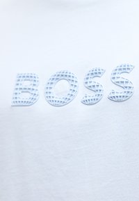 Λευκό ύφασμα με ανάγλυφα, υφή, ανοιχτό μπλε γράμματα που σχηματίζουν τη λέξη "BOSS" σε ένα μοντέρνο, πλέγμα-όμοιο μοτίβο.