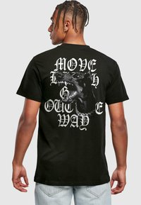 Sort bomulds T-shirt med et stort grafik af en snerrende hund og teksten "MOVE OUT THE WAY" i fede hvide bogstaver på ryggen.