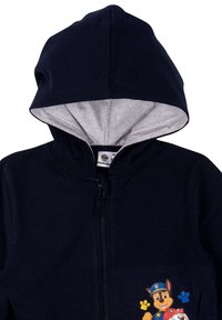 Felpa con zip color navy e fodera grigia, con personaggi di cani in cartone animato e impronte colorate sul davanti. Tessuto morbido, vestibilità standard.