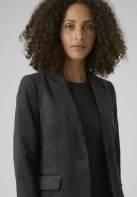 Schwarzer Cordblazer mit einem strukturierten, gerippten Design. Verfügt über einen Reverskragen und Fronttaschen, getragen über einem schwarzen Oberteil.