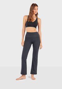 Zwarte sportbeha met witte afwerking en zwart, hooggewaisted flared broek. Gladde, elastische stof met een comfortabele pasvorm.