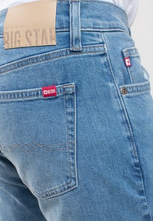 Světle modré džíny z denimu s texturovaným povrchem, které mají dvě zadní kapsy a kontrastní červenou etiketu na pravé kapse.