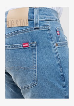 Hellblaue Jeans aus Denim mit strukturierter Oberfläche, ausgestattet mit zwei Gesäßtaschen und einem kontrastierenden roten Etikett an der rechten Tasche.