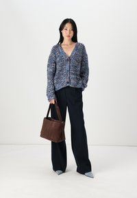 Strikket cardigan i blå og lilla nyanser, med v-hals og knappelukking. Kombinert med svarte vide bukser og en brun lærveske.