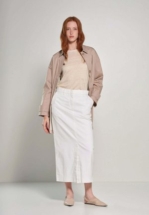 Beige trenchcoat over een lichtbruin top en een witte midi rok. Huidskleurige flats met een eenvoudig design versterken het neutrale kleurenpalet van de outfit.