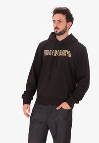 Felpa nera in cotone con cappuccio regolabile e tasca frontale. Presenta un colorato logo "DIESEL". Polsini e orlo a coste.