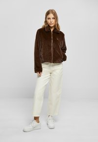 Brun, faux-pels cropped jakke med krage og glidelås. Kremfargede, løstsittende bukser og hvite joggesko fullfører antrekket.