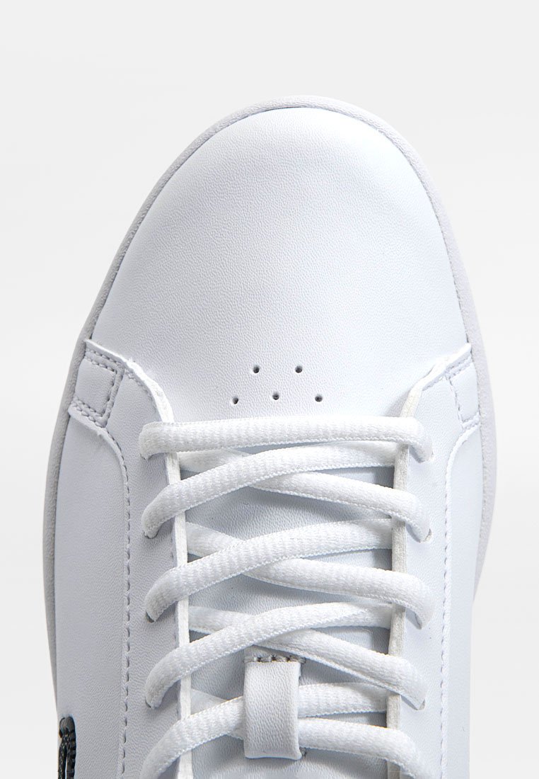 Zapatilla blanca con un upper de cuero liso, puntera redonda, seis ojales blancos y cordones planos. Presenta pequeñas perforaciones cerca de la zona de la puntera.