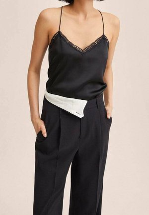 Kvinde iført en sort satin camisole med blonderkant, nedgjort i høj taljede, sorte bukser med vide ben og hvidt stofdetalje ved taljen.