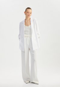 Blazer blanco de doble botonadura sobre un top de tirantes acanalado blanco y pantalones de pierna ancha. Textura suave, diseño minimalista y esquema de colores a juego.