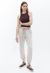Bordeaux zonder mouwen top gecombineerd met lichtbeige joggers met elastische tailleband, voorzien van zijzakken en verzamelde manchetten. Bruine sneakers maken de look compleet.