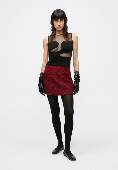 Czarny siateczkowy top na ramiączkach z wycięciami, czerwona teksturowana mini spódnica, czarne rękawiczki, czarne rajstopy i czarne baleriny, prezentujące wielowarstwowy design.