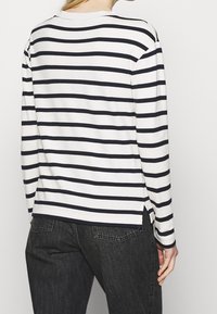 Camicia a maniche lunghe a righe in crema e blu navy, con colletto a girocollo, fessure laterali e vestibilità rilassata. Tessuto morbido con una consistenza liscia.