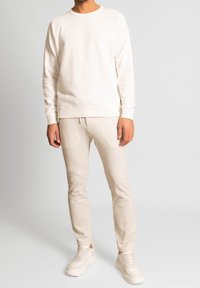 Světlý béžový svetr s žebrovanými manžetami, doplněný o odpovídající zúžené kalhoty. Oba kusy jsou vyrobeny z měkkého materiálu, mají jednoduchý design a žádné vzory.