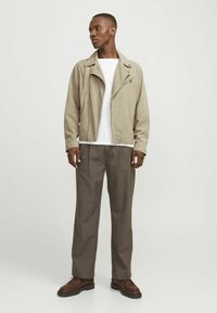 Beige velúr motoros dzseki cipzárral az elején, alatta fehér póló, és barna nadrág. Barna cipők egészítik ki az outfitet.