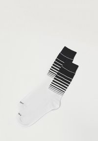 Calcetines de rayas en blanco y negro con un tobillo negro sólido, rayas en contraste y una textura suave, diseñados para la comodidad y el estilo.