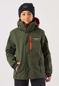 Grön softshelljacka med huva, med orangea detaljer, dragkedjeförsedda fickor och en logga på bröstet. Svart mössa på modellens huvud.