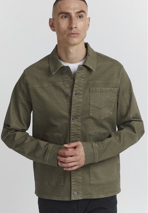 Olive green jacket made of sturdy fabric, featuring a button front, chest pocket, and side pockets. Textured surface with visible stitching.
