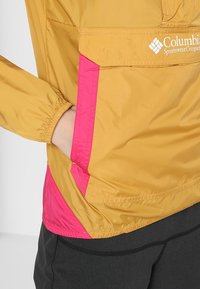 Giacca leggera gialla con un accento rosa, con polsini elasticizzati e una tasca frontale. Realizzata in tessuto morbido e resistente.