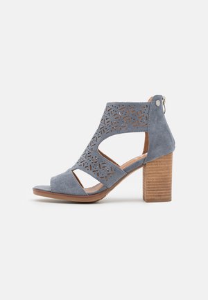 Sandale à talon haut ouverte à l'avant en daim gris avec côtés ajourés, motifs découpés au laser, talon bloc en bois et fermeture éclair à l'arrière.