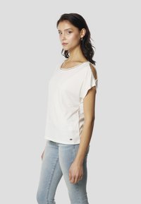 Valge lühikeste varrukatega top ringkaelusega, millel on õlgadel lõigatud detailid ja väiksed mustad aksendid kaeluse ääres. Pehme kangas.